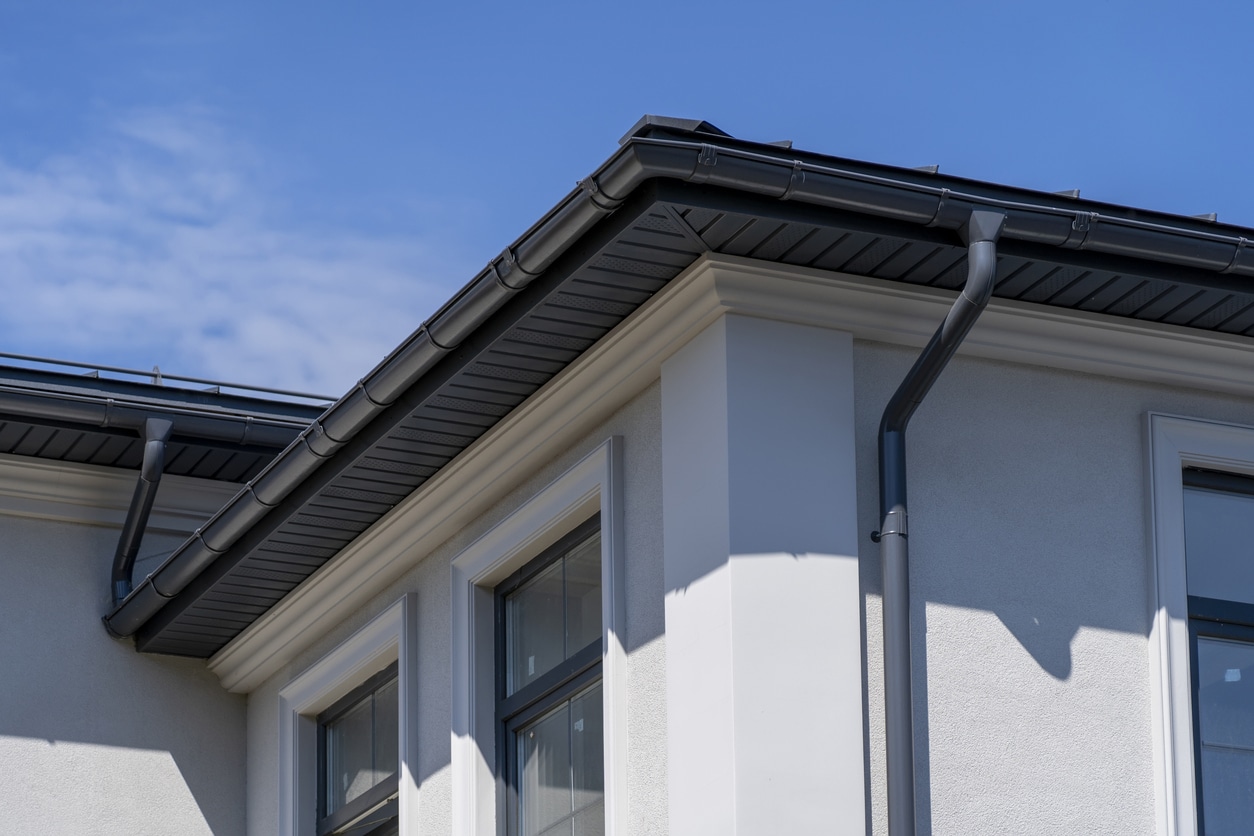 Corner of house with windows, new gray metal tile roof and rain gutter. Metallic Guttering System, Guttering and Drainage Pipe Exterior Corner of house with windows, new gray metal tile roof and rain gutter. Metallic Guttering System, Guttering and Drainage Pipe Exterior