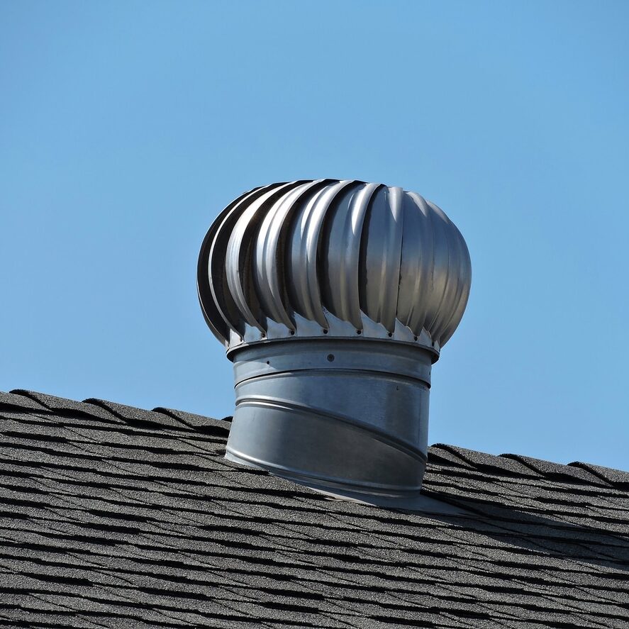 Silver colored wind turbine of a rooftop against a clear blue sky.